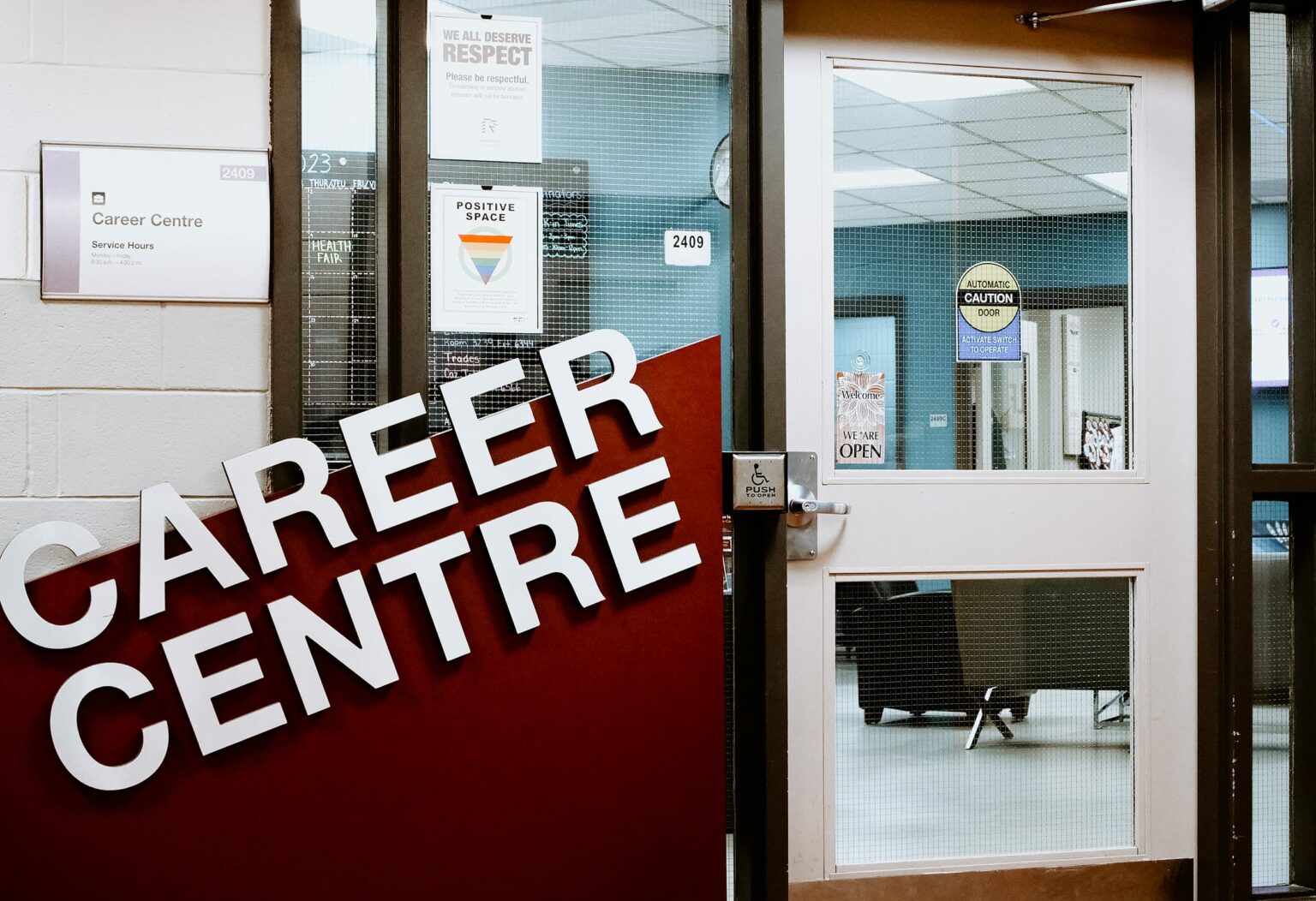 Entrance to Cambrian's Career Centre with a large sign, glass doors, and visible office interior. Signs on the door include "Respect" and "Positive Space.