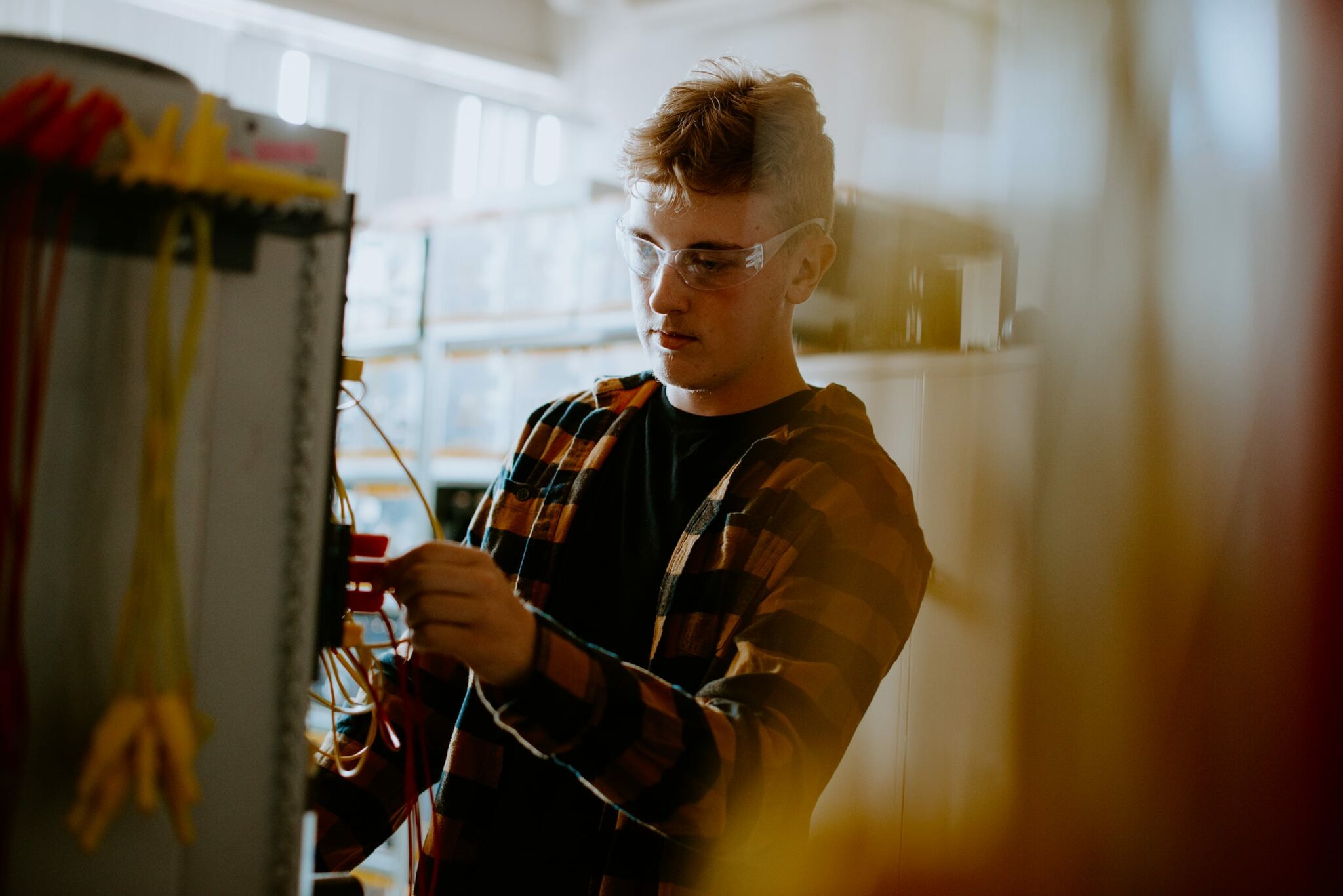 A student wearing safety glasses works with wiring in a technical setting.