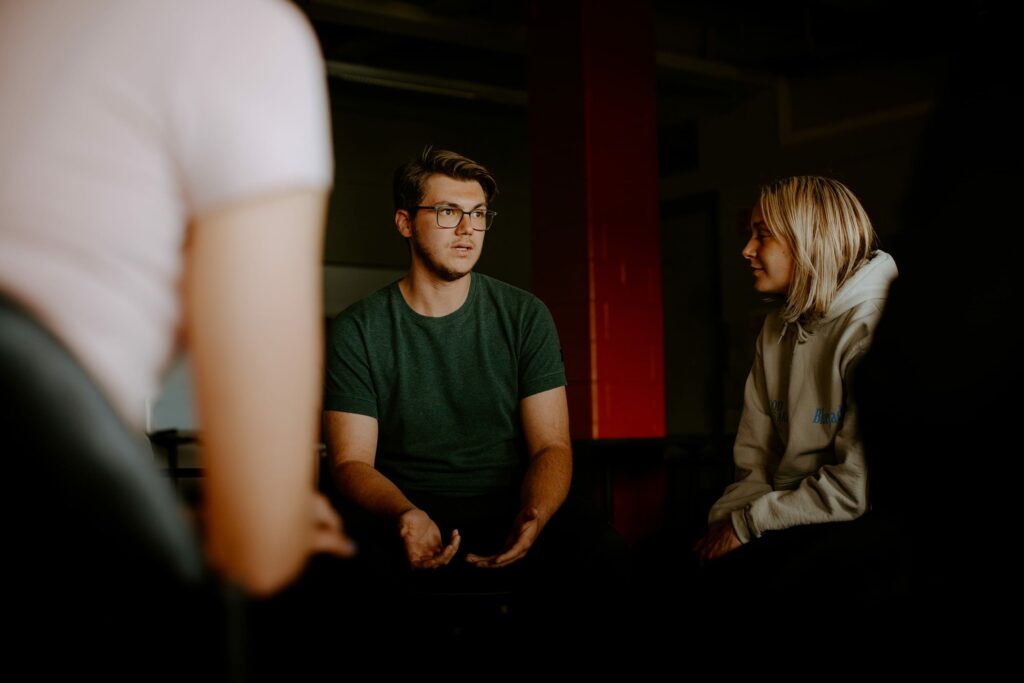 A group of students sitting and talking in a dimly lit indoor setting.
