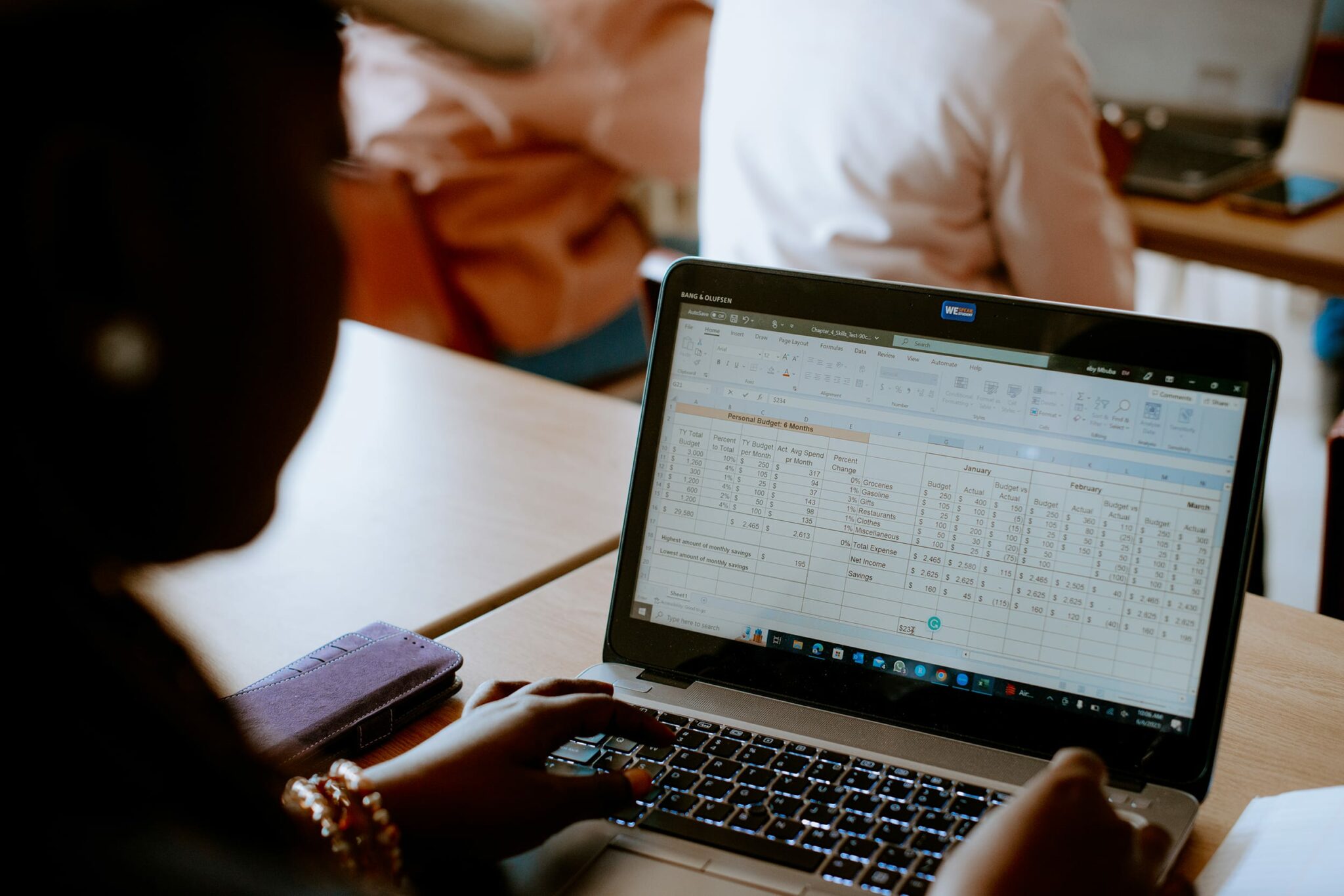 A student uses a laptop with a spreadsheet open, showing rows of numerical data.