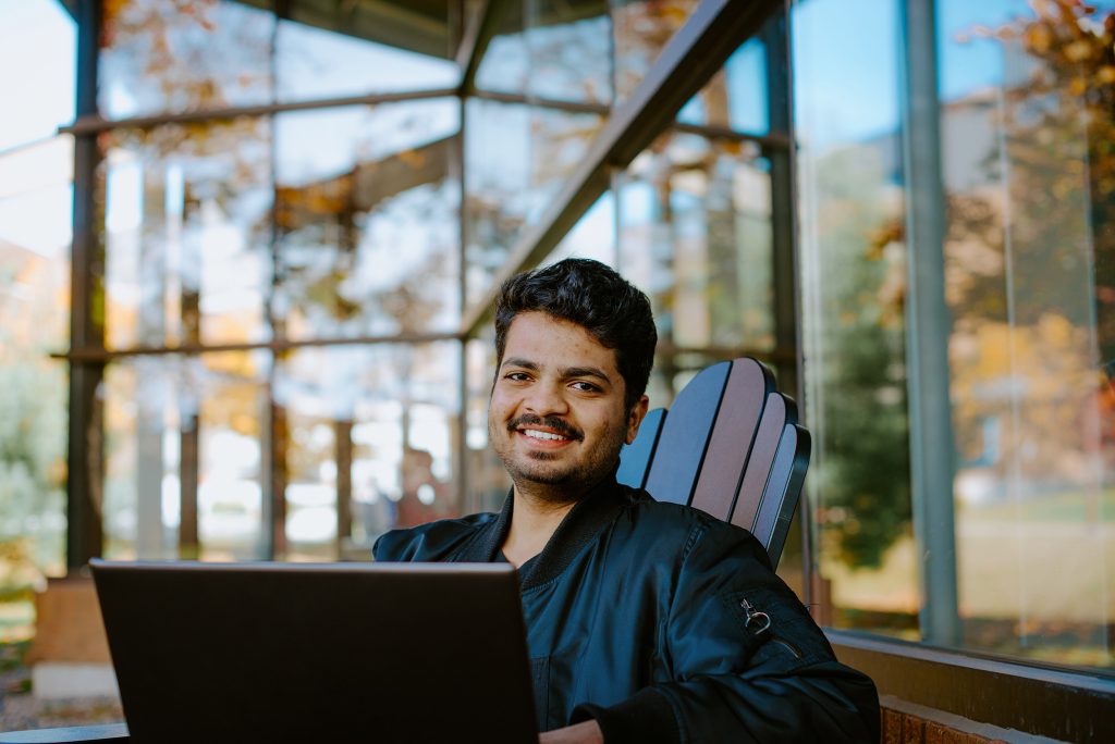 Student sitting on a chair, using a laptop outside on campus