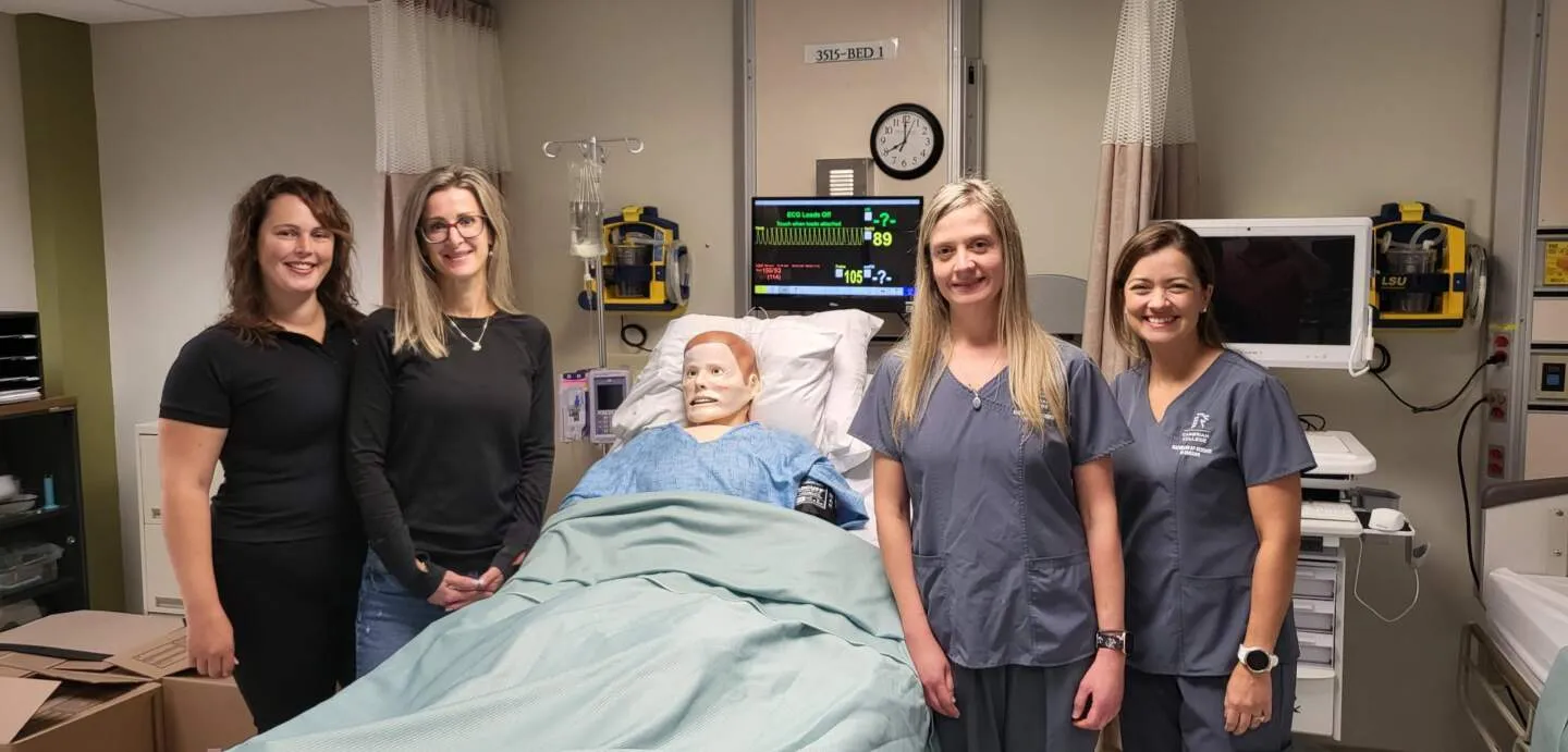 Four women stand beside a medical mannequin in a hospital simulation room, surrounded by cutting-edge medical equipment and monitors. At Cambrian College, students in health care programs gain hands-on experience that brings their education to life.