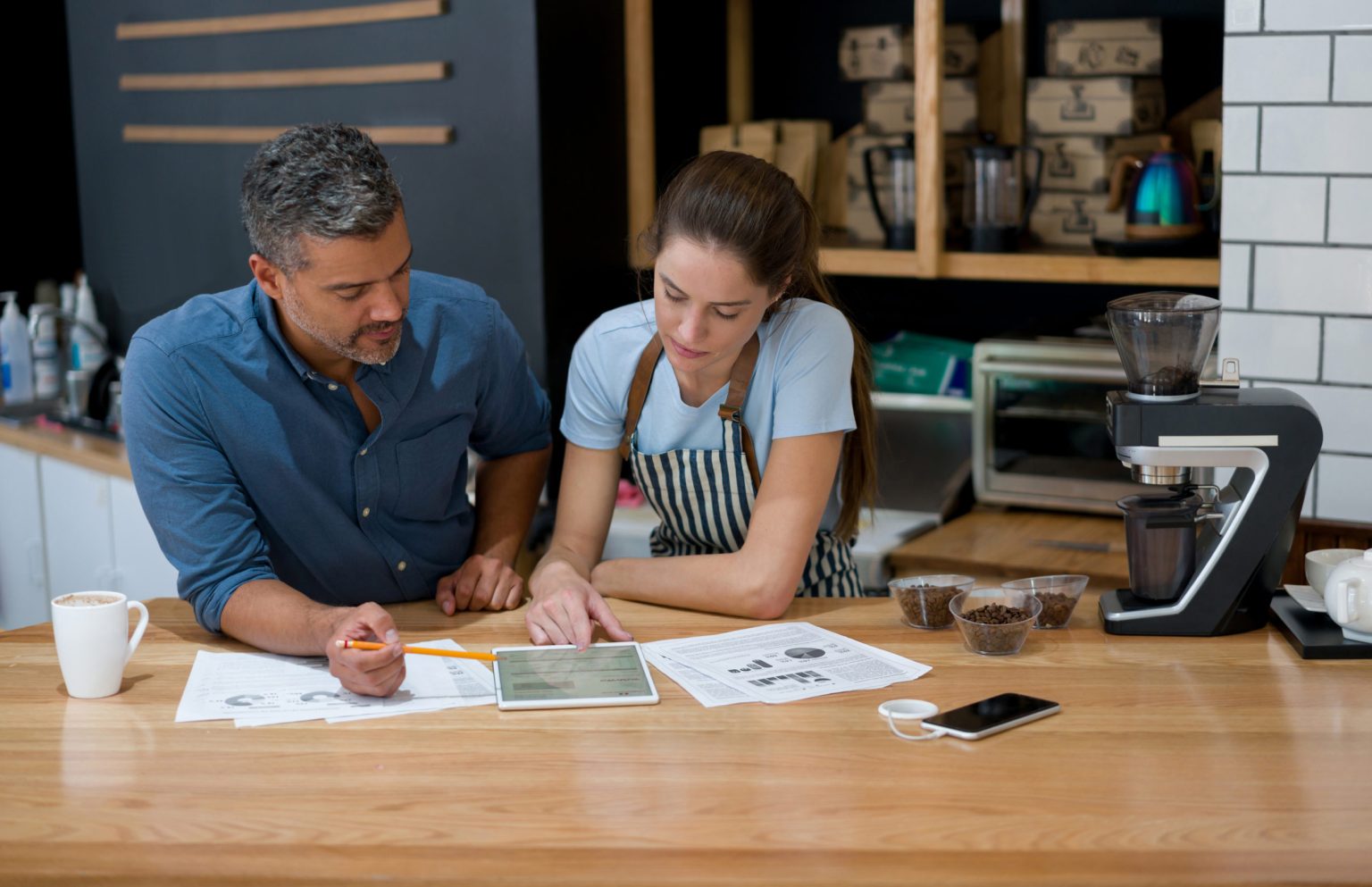 Man and woman in a coffee shop looking at an tablet working on budgets.