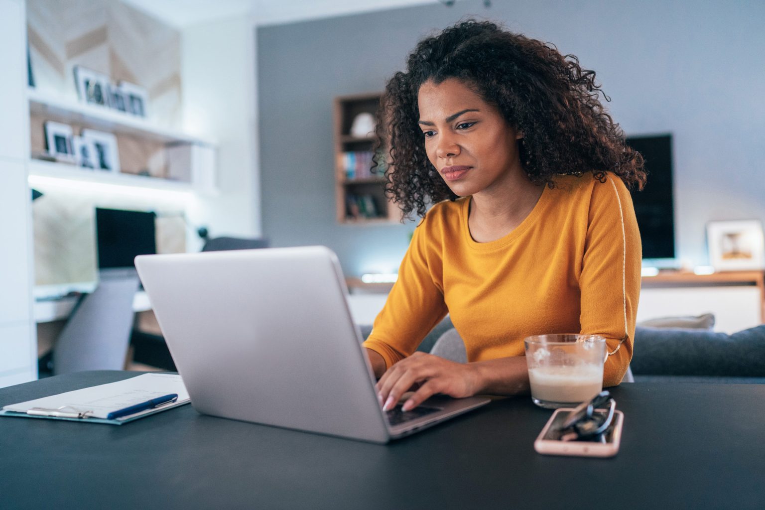 Woman working from home on a laptop typing with a coffee next to her.