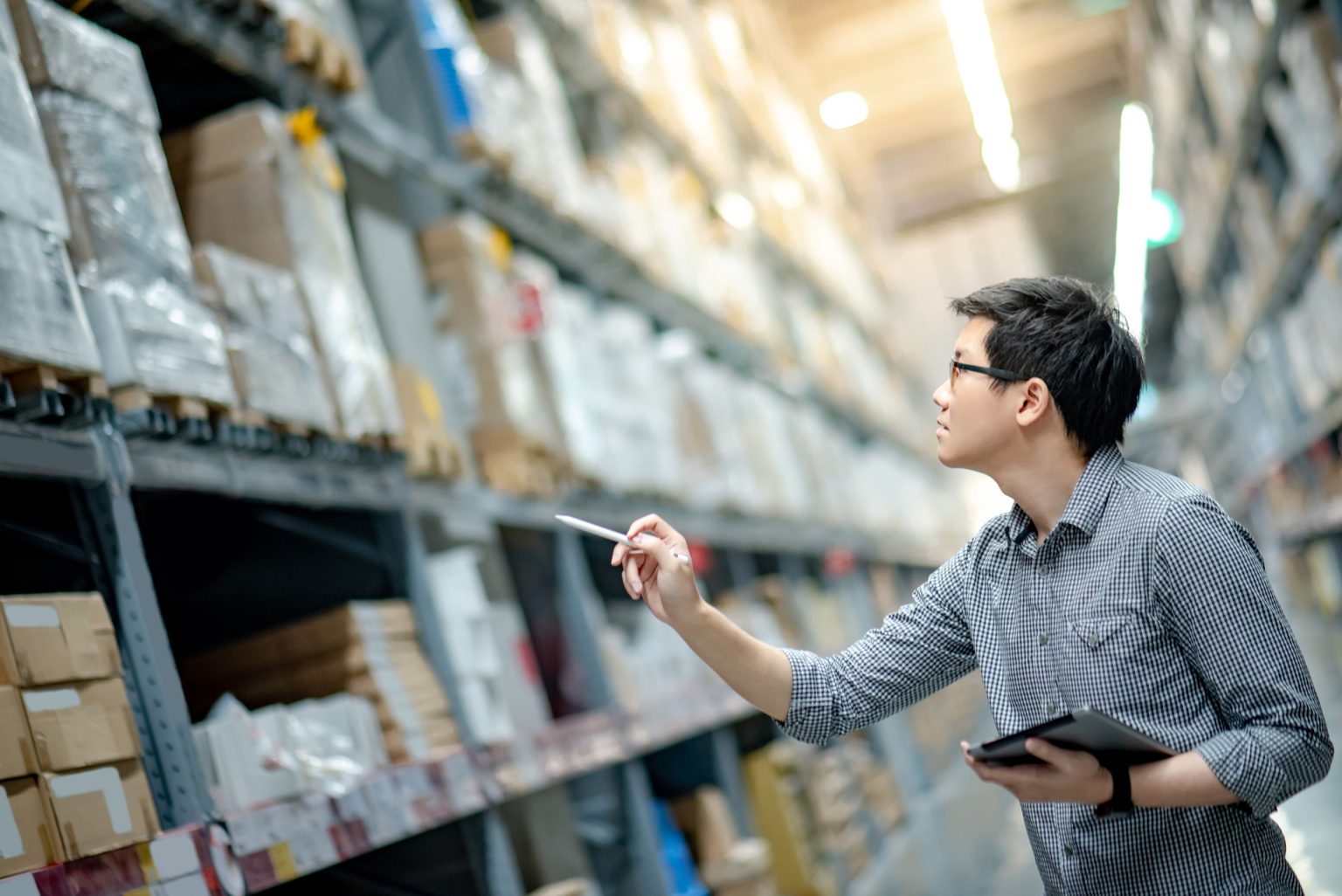 Man worker in a warehouse pointing at the shelves with a tablet in their hands.