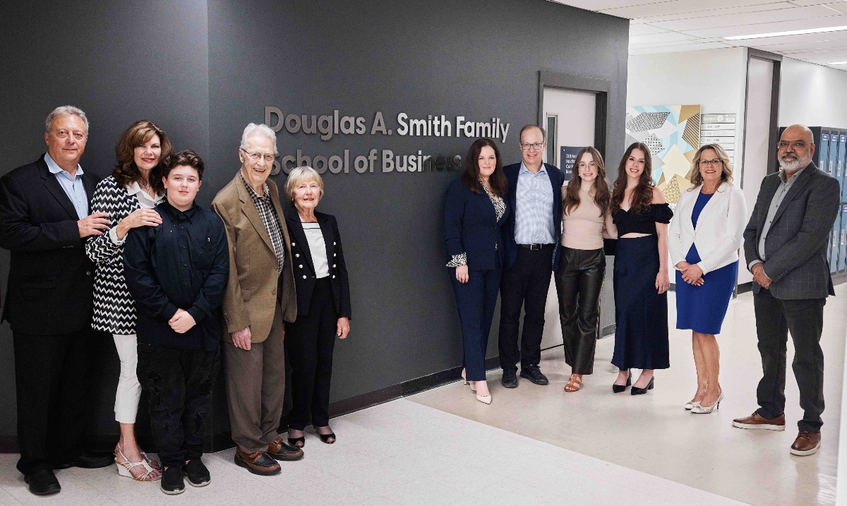 A group of people stands in a hallway beside a sign that reads "Douglas A. Smith Family School of Business" at Cambrian College.