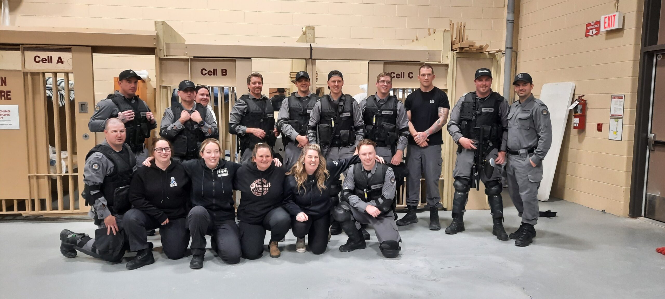 Group photo of uniformed officers and staff members in a building with labeled doors behind them, representing the Sudbury Jail's Crisis Intervention Team.