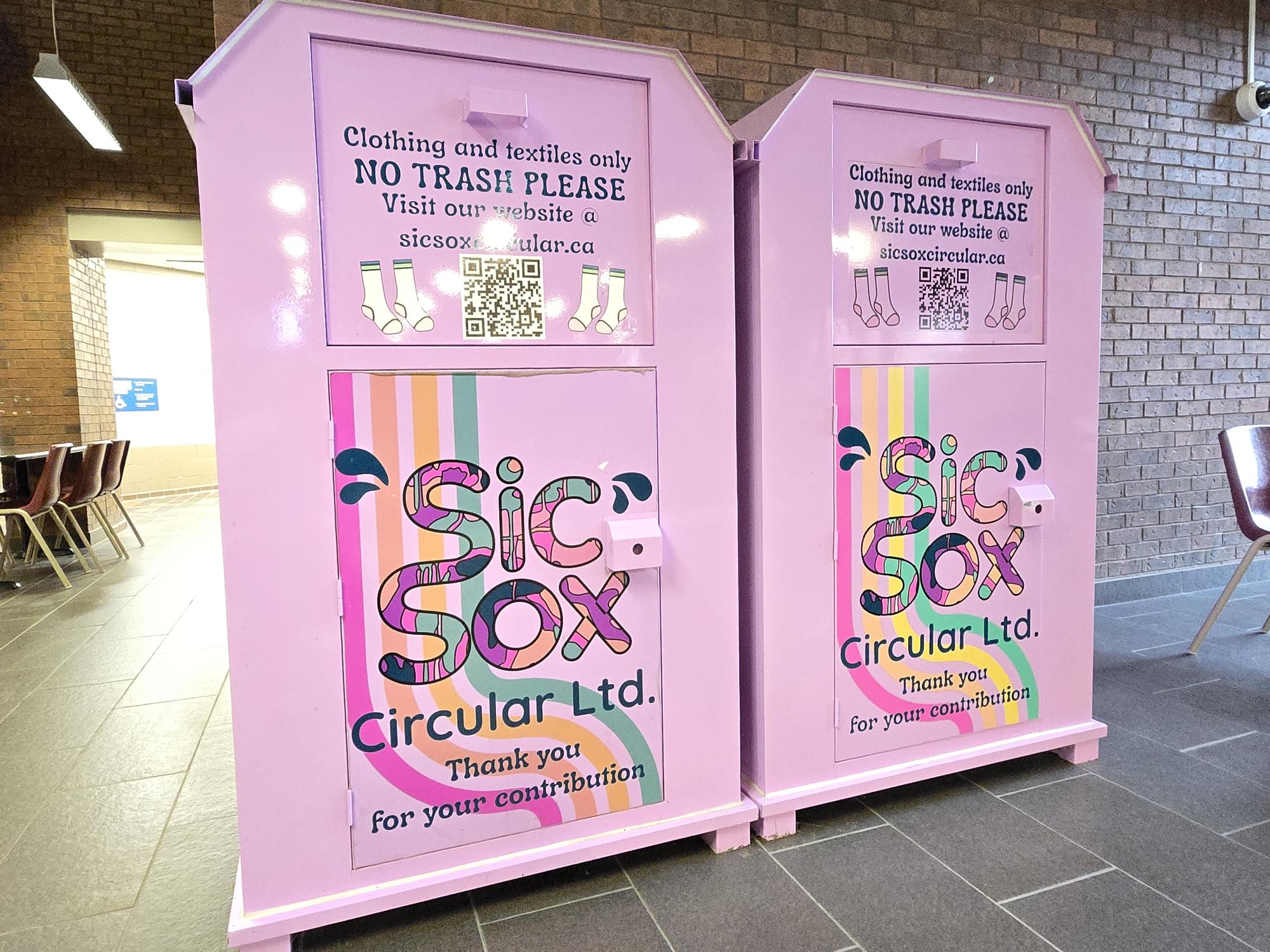 Two pink clothing donation bins with "Sic Sox Circular Ltd." branding stand proudly, urging passersby to help reduce their carbon footprint. The bins, located near Cambrian College, kindly request no trash talking—let's keep it clean and sustainable for the future!.
