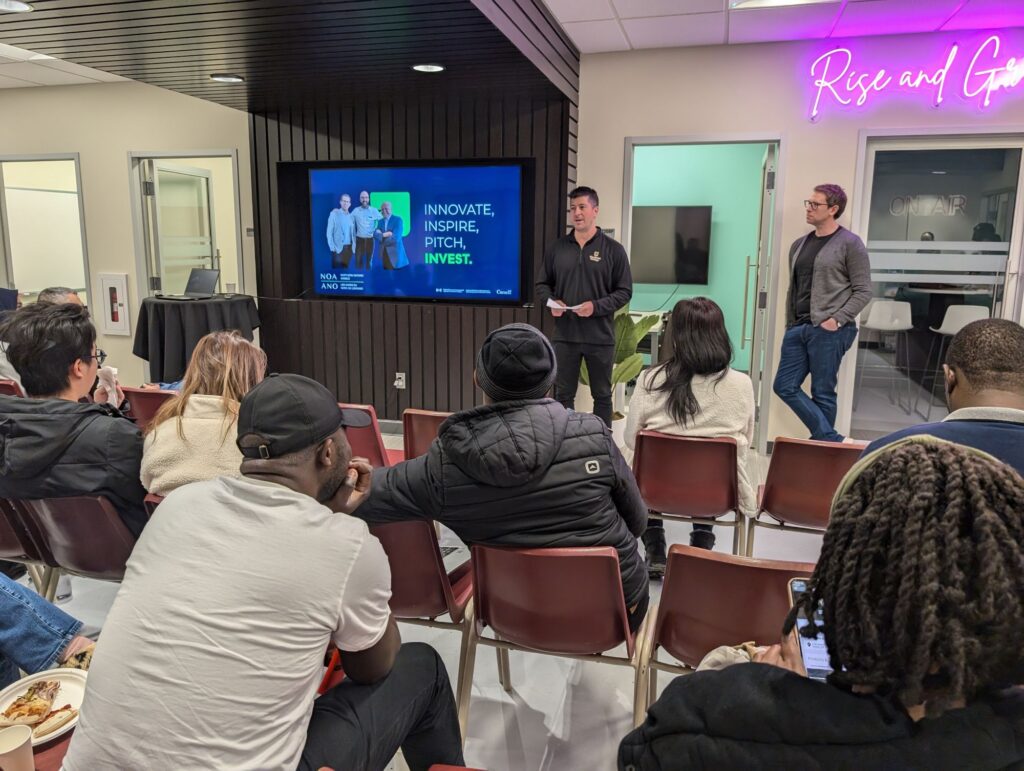 A group of people sit facing two men presenting in front of a screen displaying the text "Innovate. Inspire. Pitch. Invest." at the Hanson Venture Lab's modern office space.
