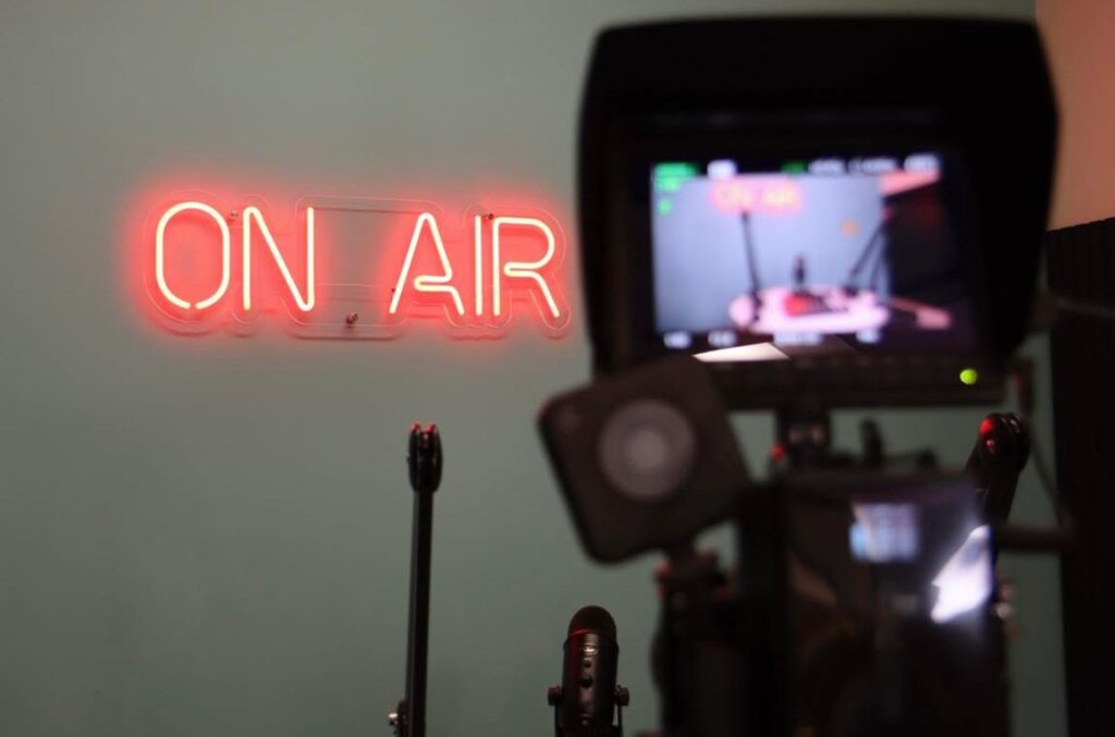 A red neon "ON AIR" sign glows on a wall at Hanson Venture Lab, with a video camera and monitor in the foreground showing a recording setup.