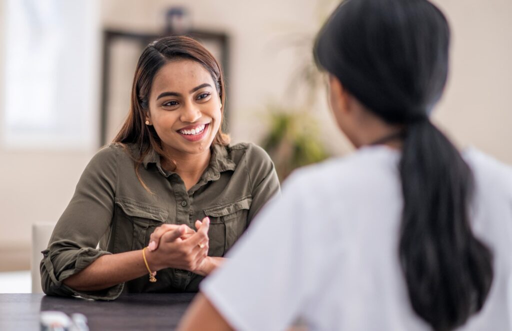 A student smiles and talks with a healthcare professional across a table in a well-lit room.