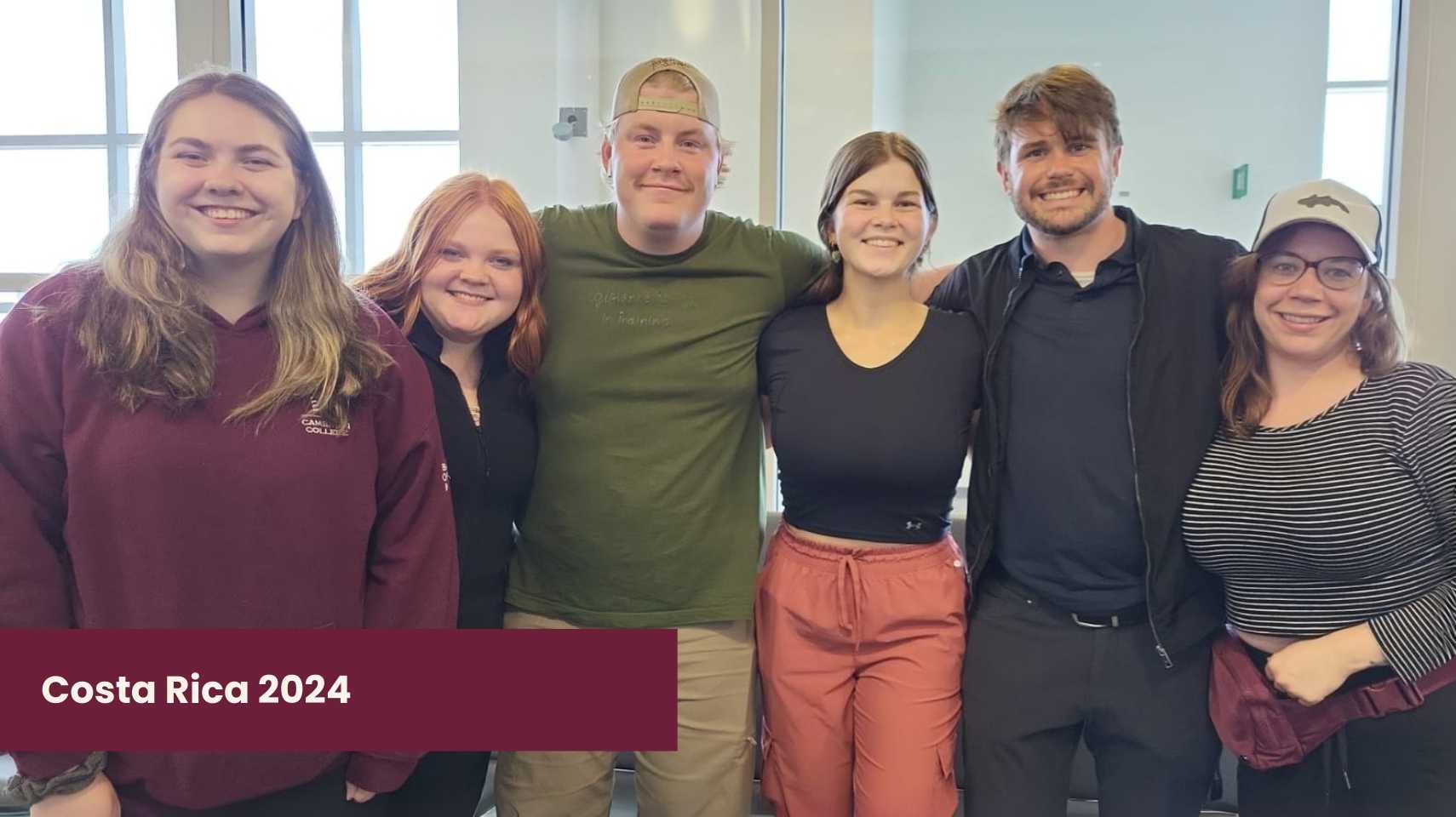 Six smiling students stand together indoors, posing for a group photo. A maroon banner in the corner reads "Costa Rica 2024," highlighting their Cambrian College Global Skills Opportunity experience.