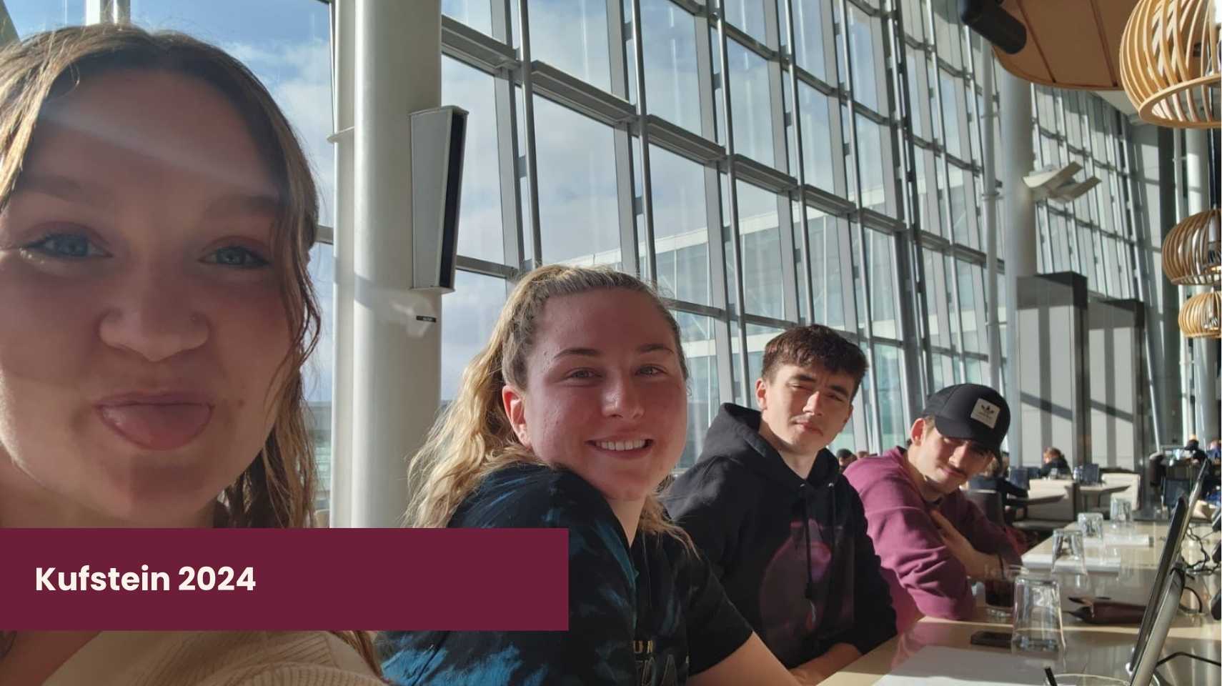 Four young students sit at a table in a modern, sunlit building with large windows. A label in the corner reads "Kufstein 2024," highlighting their Cambrian College Global Skills Opportunity experience abroad.