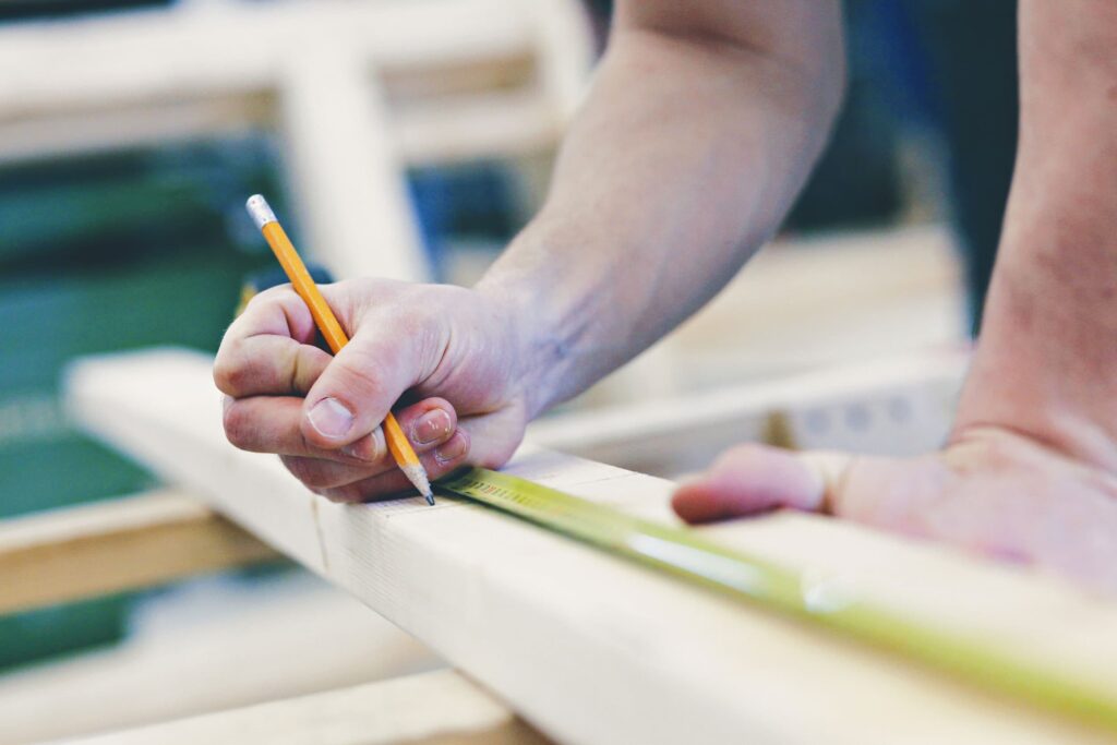 A student uses a pencil and tape measure to mark measurements on a piece of wood.