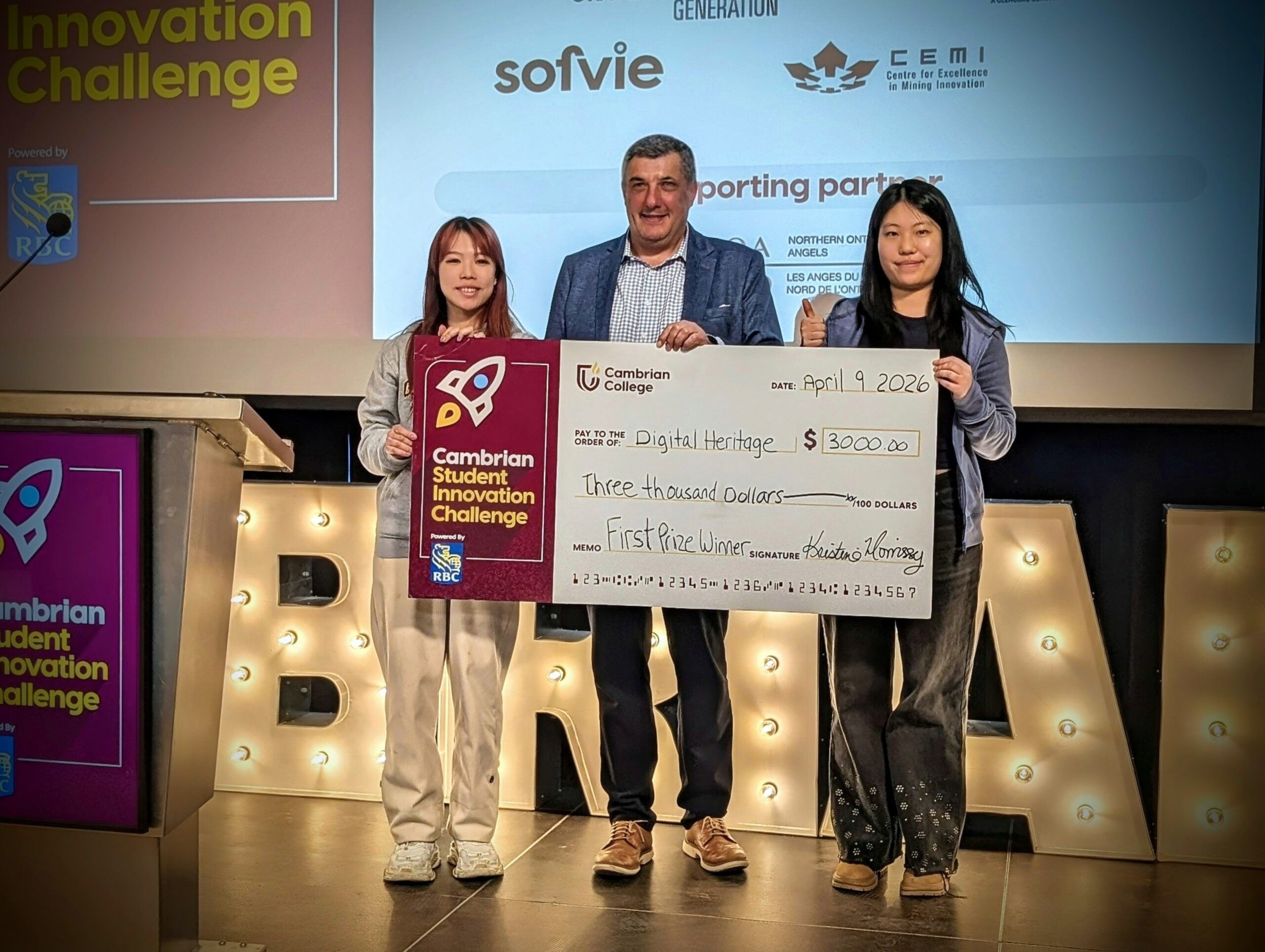 Three people stand on stage holding an oversized $3,000 check for winning first prize at the Cambrian Student Innovation Challenge on April 9, 2026.