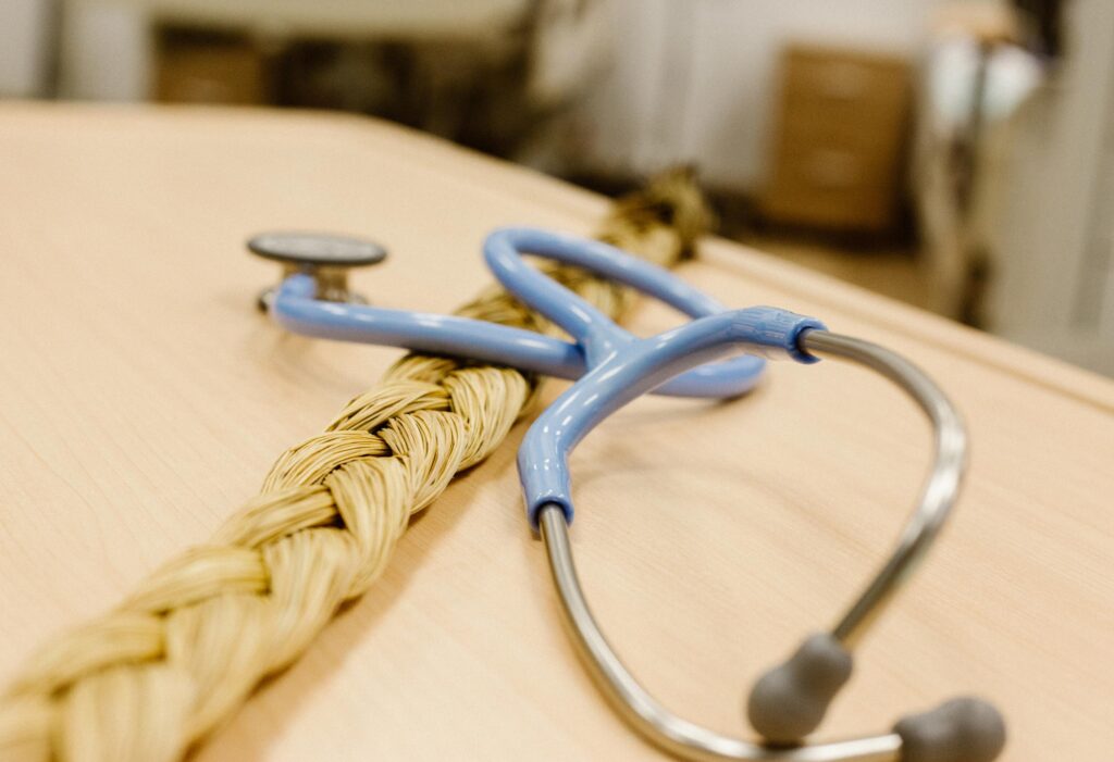 A blue stethoscope and a braided straw rope lie on a light wooden surface, with a blurred background of a room.