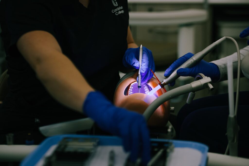 A person wearing blue gloves performs a dental procedure on a patient using dental instruments under bright light.
