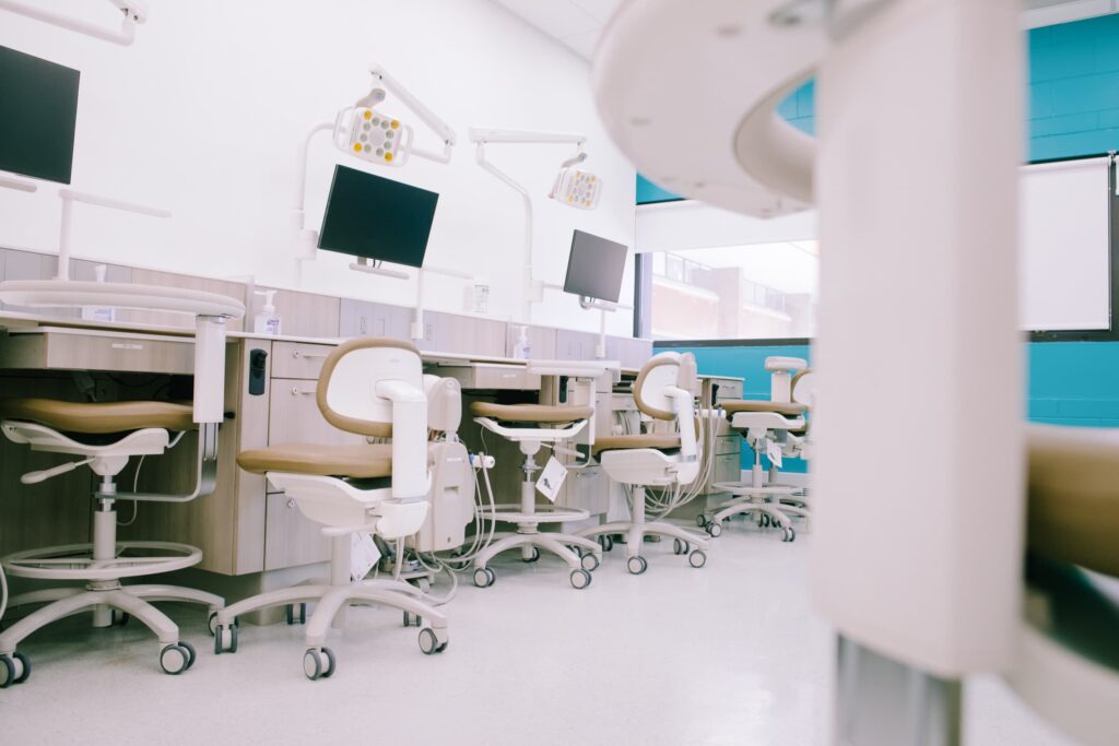 Empty dental workstations with adjustable chairs, monitors, and dental equipment arranged in a clean, modern clinical setting.