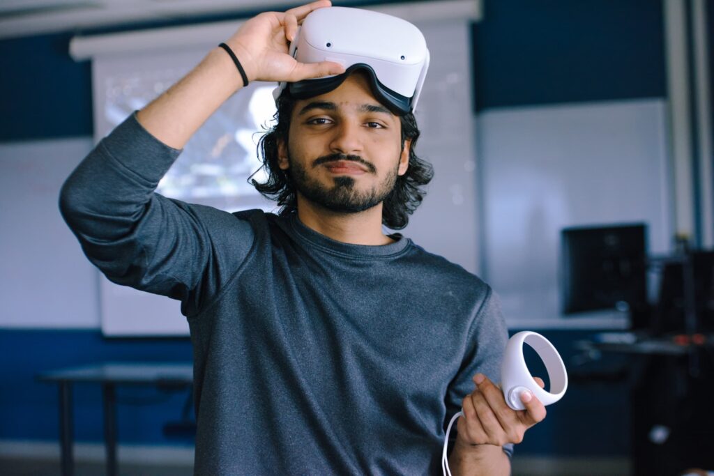 A person lifts a virtual reality headset above their eyes and holds a VR controller in one hand, standing in a classroom or office setting.