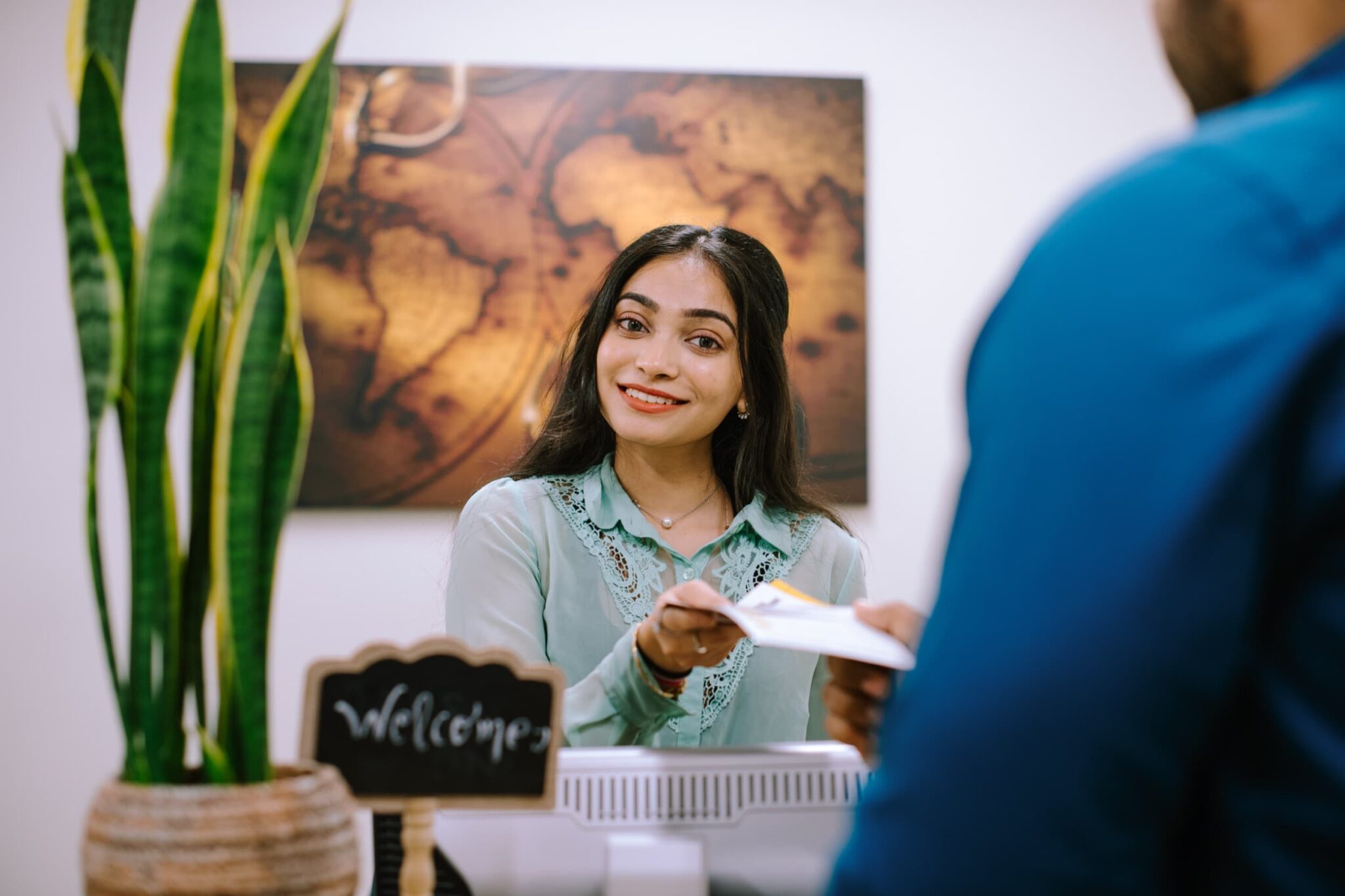 A smiling support staff hands a brochure to a student at a front desk.
