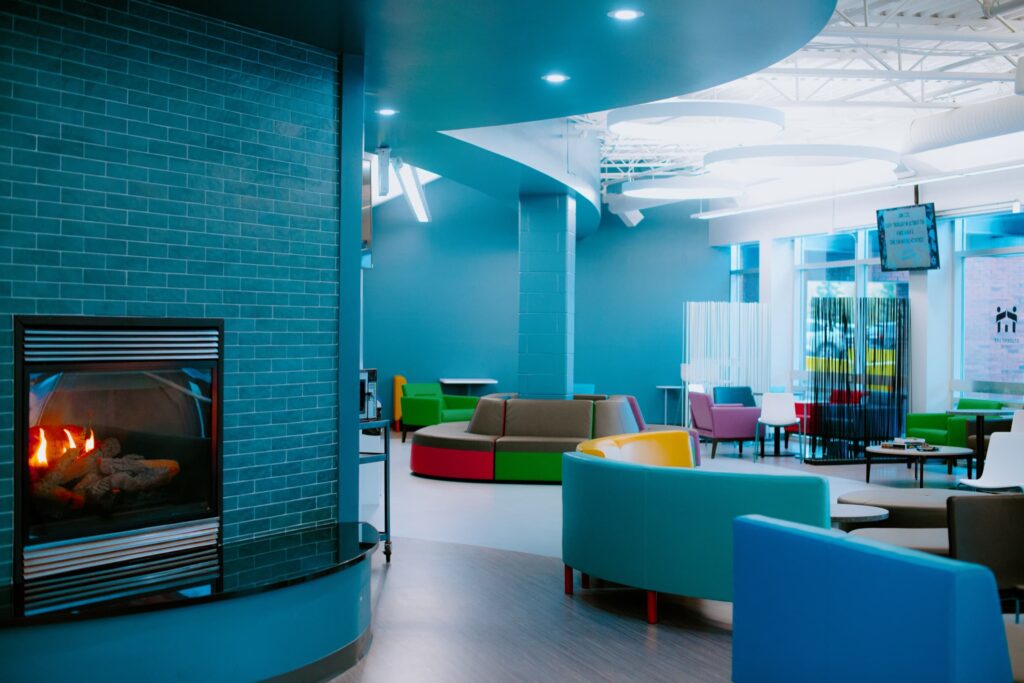 A brightly colored modern lounge area with curved modular seating and a built-in fireplace on a teal tiled wall.