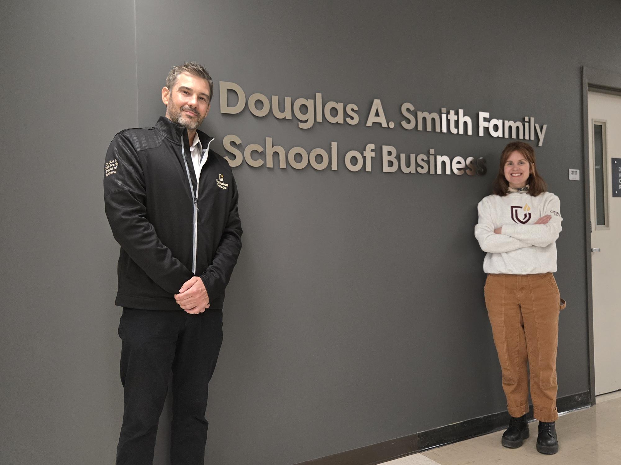 Cambrian professors Craig O'Neill and Kristeen McKee stand in front of the sign for the Douglas A. Smith Family School of Business at Cambrian College